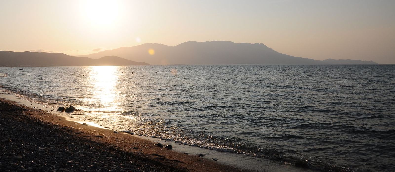 夕方の岩の多い海岸と、向こうに連なる山